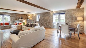 A spacious living area with a stone wall, wooden beams, a sofa set, a dining table with chairs, and a lamp. - Eido do Carvalhoso (Arcos de Valdevez)