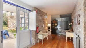 A room with a stone wall, a wooden floor, a white door, a fire extinguisher, a small table with a lamp, and a radiator. - Eido do Carvalhoso (Arcos de Valdevez)