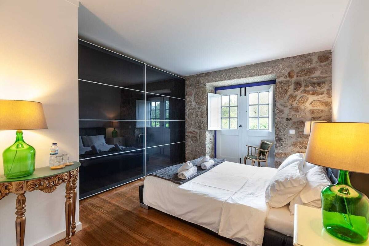 Een moderne slaapkamer met een groot bed, een glazen scheiding, een stenen muur en een raam.