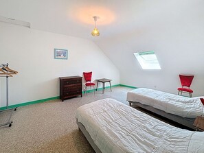 A room with two beds, a dresser, a chair, a small table, and a hanging light fixture.