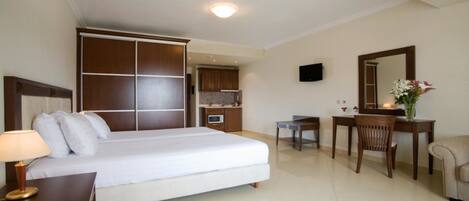 A hotel room with a large bed, a desk, a chair, a television, and a small kitchenette.