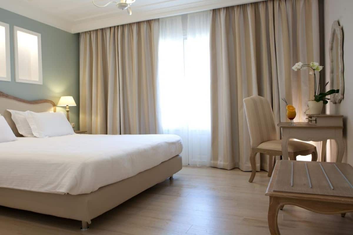 Una habitación de hotel con una cama grande, un escritorio, una silla y una ventana con cortinas.