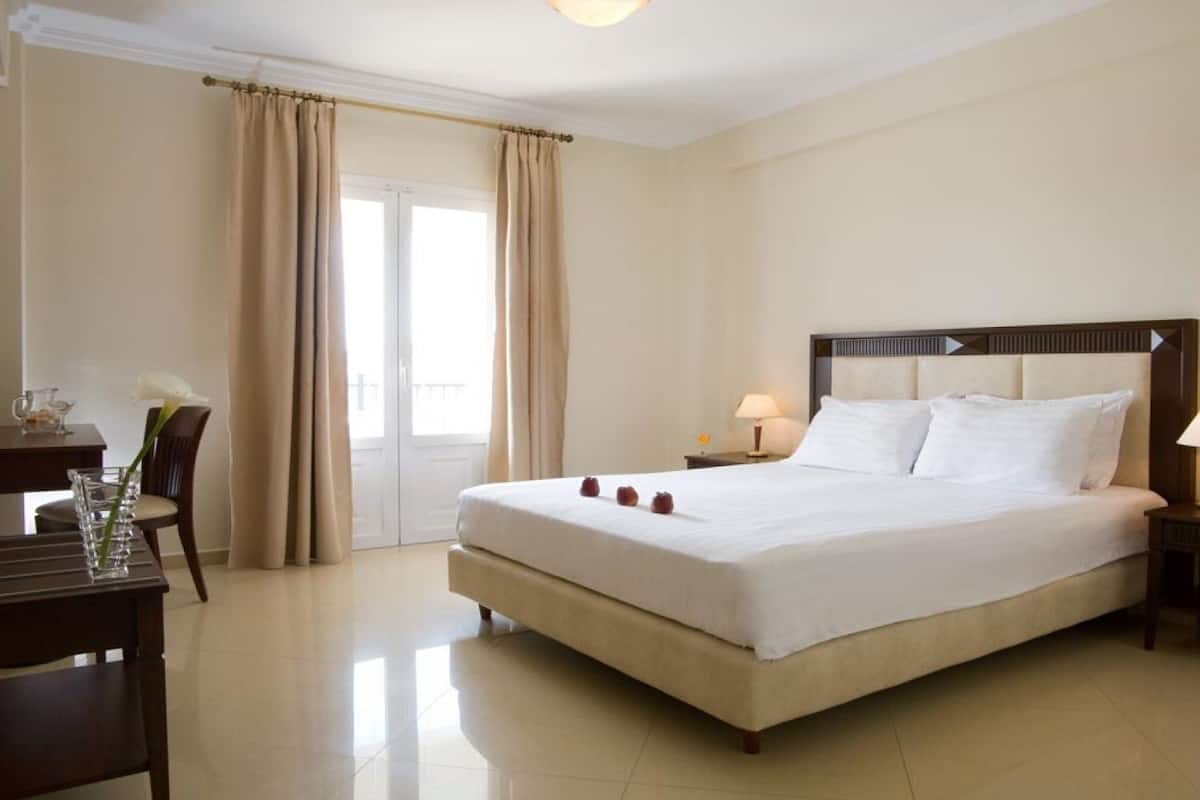 Habitación de hotel con una cama grande, un escritorio con silla, una mesita y una mesita de noche con lámpara.