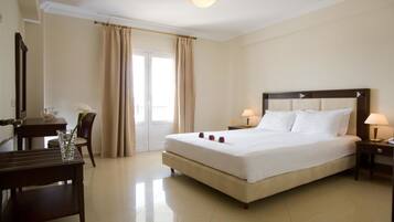A hotel room with a large bed, a desk with a chair, a small table, and a nightstand with a lamp.