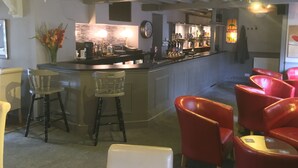 A bar area with stools, a counter with bottles, and a clock on the wall.