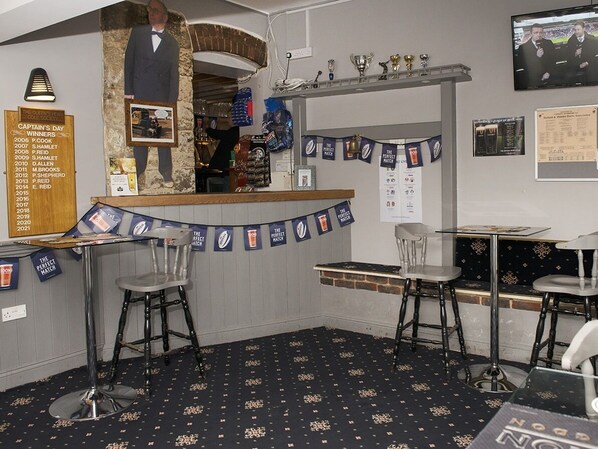 A bar area with a counter, stools, and a banner. A list of winners is displayed on the wall. - The Queens Head (Oxford)