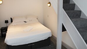 A bedroom with a bed, a nightstand, a lamp, and a staircase.