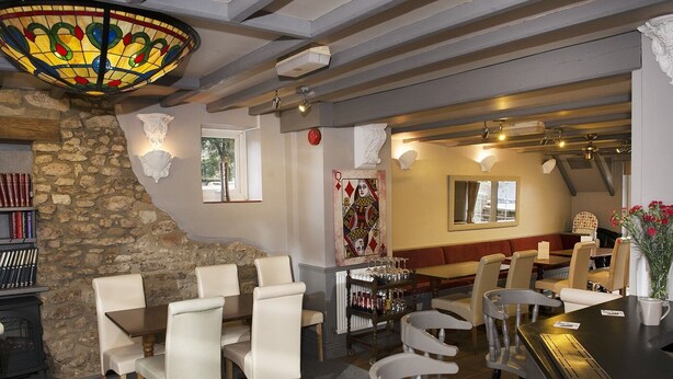 A restaurant with a stone wall, white chairs, a bar area, and a stained glass ceiling.