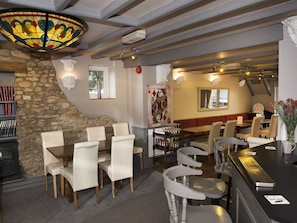 A restaurant with a stone wall, white chairs, a bar area, and a stained glass ceiling. - The Queens Head (Oxford)
