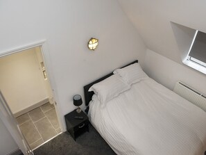 A bedroom with a bed, bedside table, lamp, and a wall-mounted light fixture. - The Queens Head (Oxford)