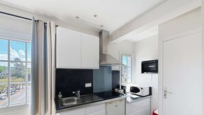 A compact kitchen with white cabinets, a black countertop, a stainless steel sink, a microwave, and a stove. - Cozy Apartment 100m from Beach & Shops, Near Mont Saint-Michel (Jullouville)