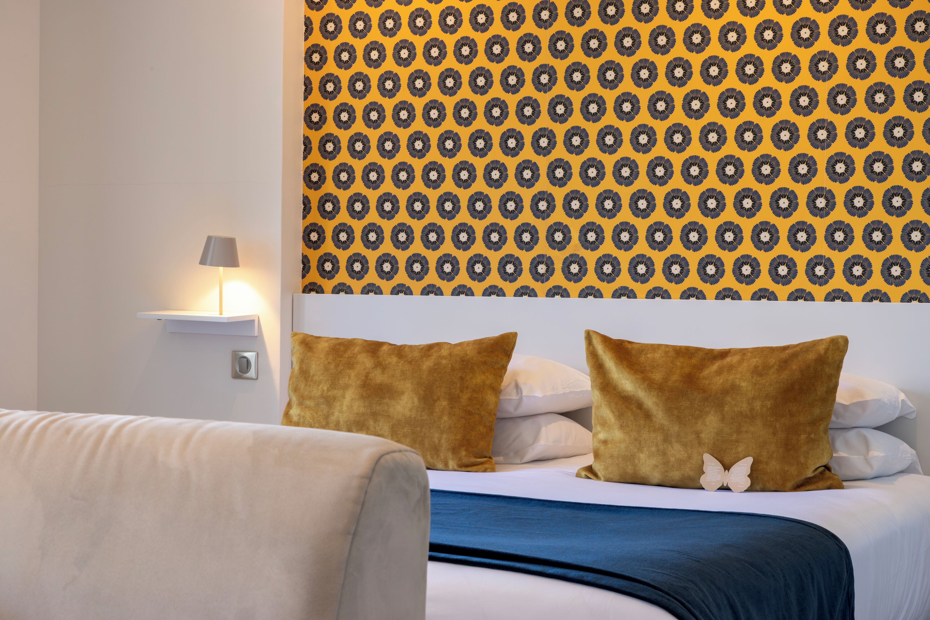 Ein Hotelzimmer mit gestreiftem Wandteppich, einem Bett mit weißer und blauer Bettwäsche und einem Nachttisch mit Lampe.