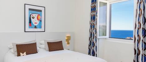 A bedroom with a bed, a framed artwork, a window with curtains, and a wall-mounted light.