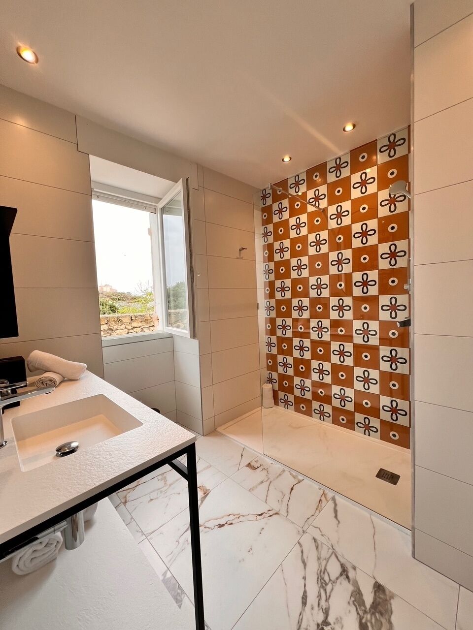 Un baño moderno con un lavamanos grande, ducha con azulejos estampados y vistas a través de una ventana.
