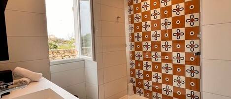 Un baño moderno con un lavamanos grande, ducha con azulejos estampados y vistas a través de una ventana.