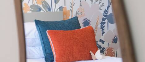 Cama com roupa de cama branca, um travesseiro azul e um travesseiro laranja.