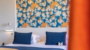 A hotel room with a bed, two pillows, a wall-mounted lamp, and a decorative wall hanging.