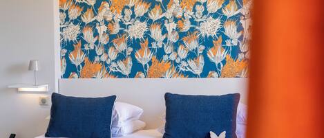 A hotel room with a bed, two pillows, a wall-mounted lamp, and a decorative wall hanging.