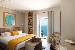 Ein Hotelzimmer mit einem Bett, einer Bank, einem Stuhl und Meerblick.