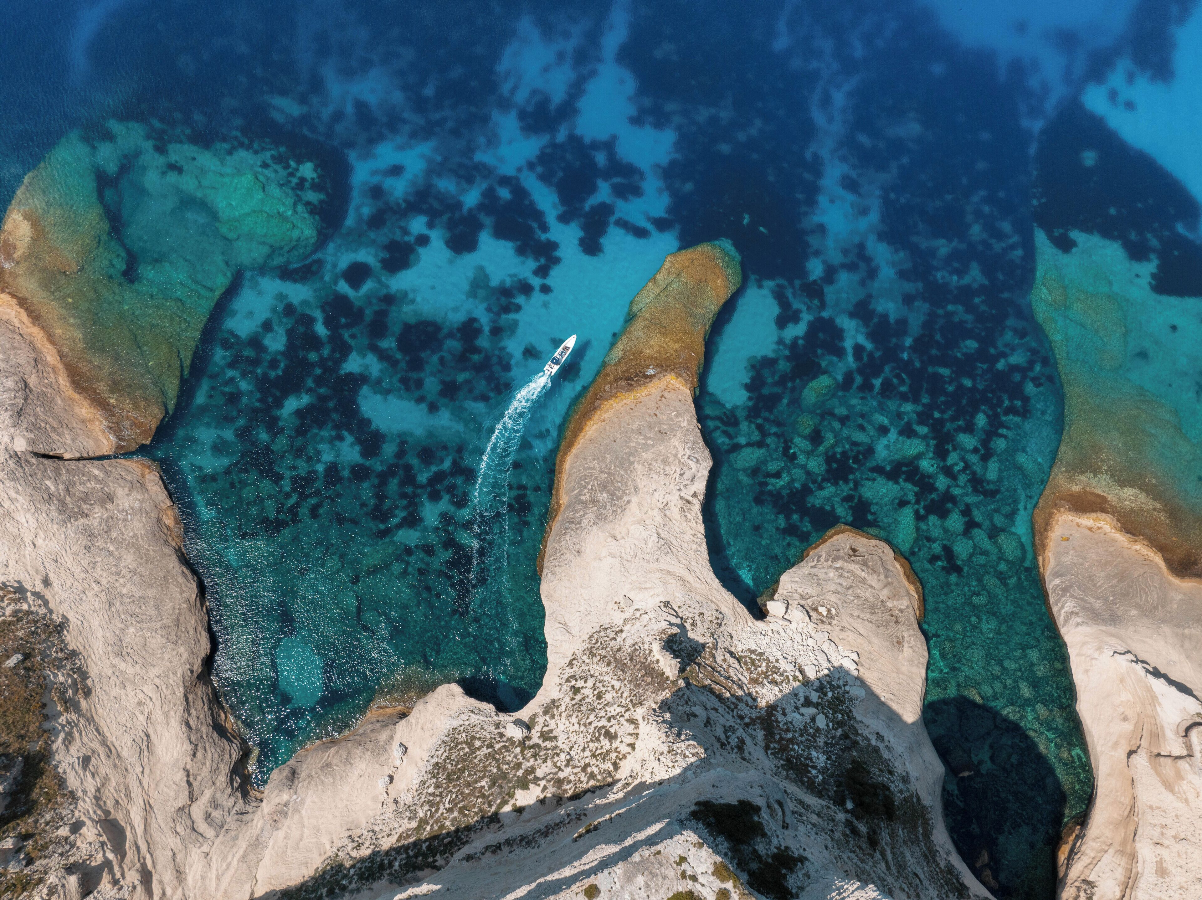 A coastal landscape with clear blue waters, rocky formations, and a boat creating a wake.