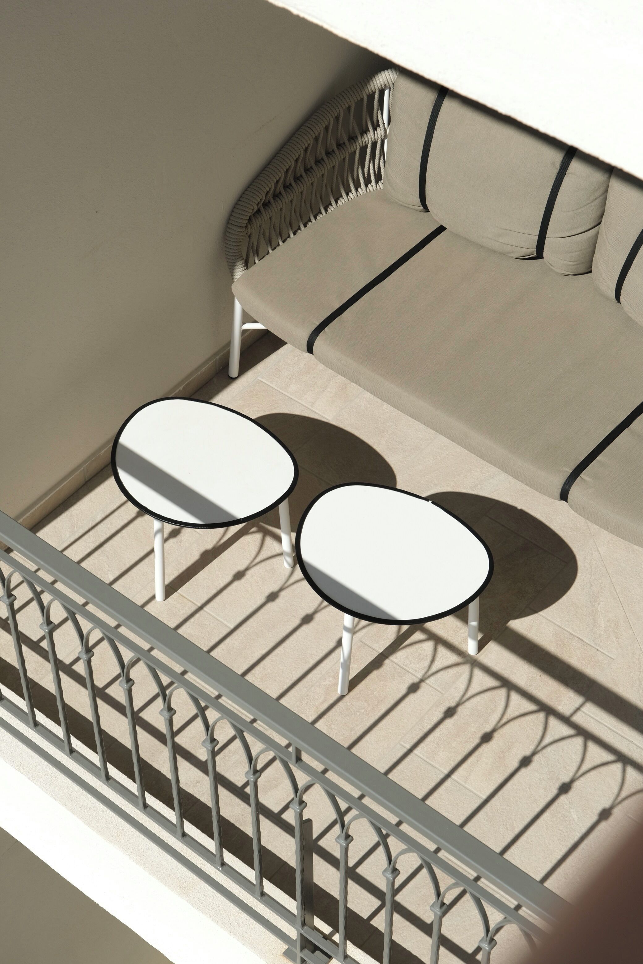 A balcony with a sofa and two tables, a metal railing, and a patterned headboard.
