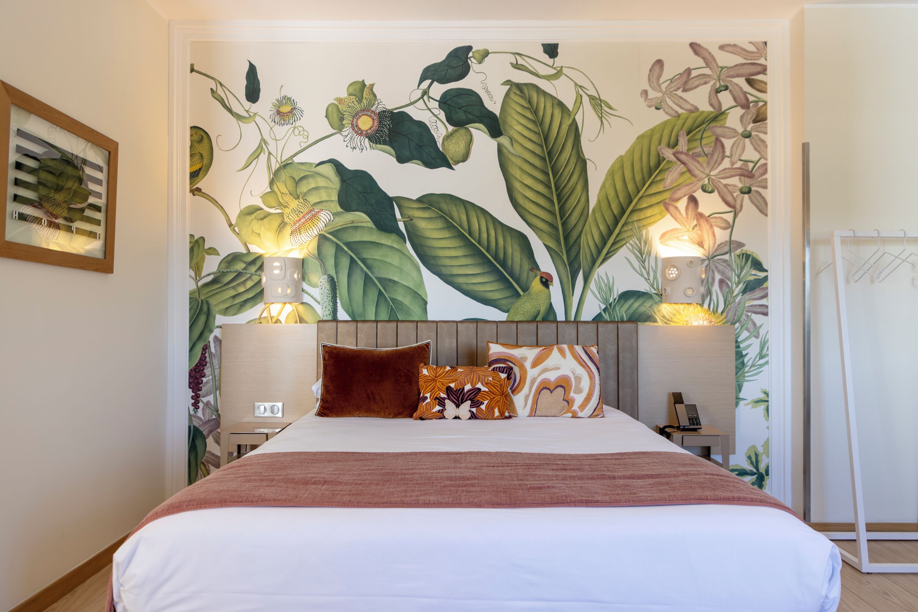 Quarto de hotel com uma cama grande, duas luminárias de cabeceira, uma mesinha de cabeceira e um mural na parede.