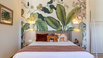 Quarto de hotel com uma cama grande, duas luminárias de cabeceira, uma mesinha de cabeceira e um mural na parede.