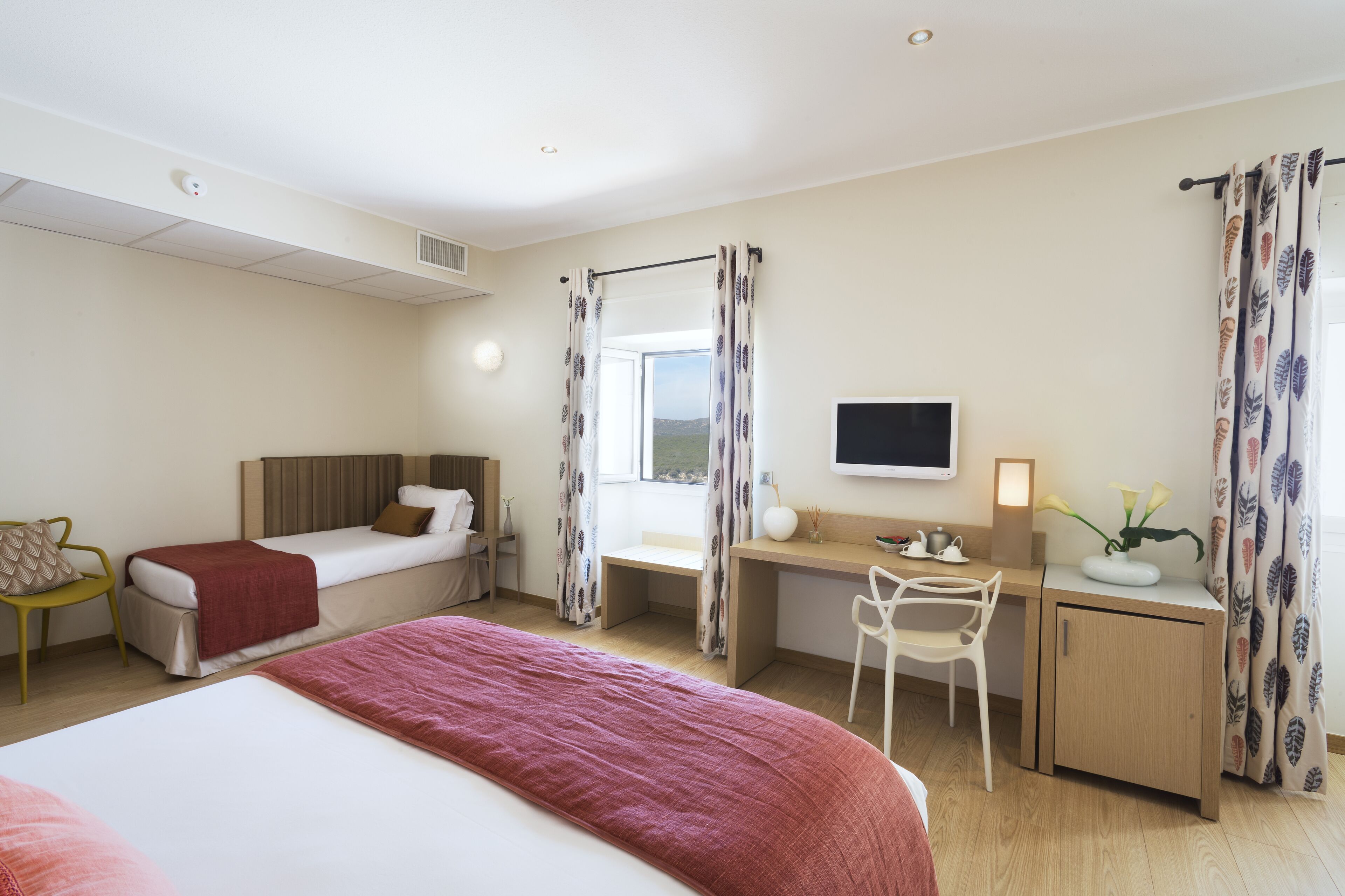 A hotel room with two beds, a desk, a chair, a TV, and a window with curtains.