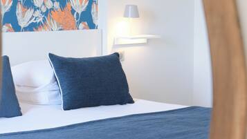A neatly made bed with a blue blanket and pillows, a wall-mounted light, and a floral-patterned wall.