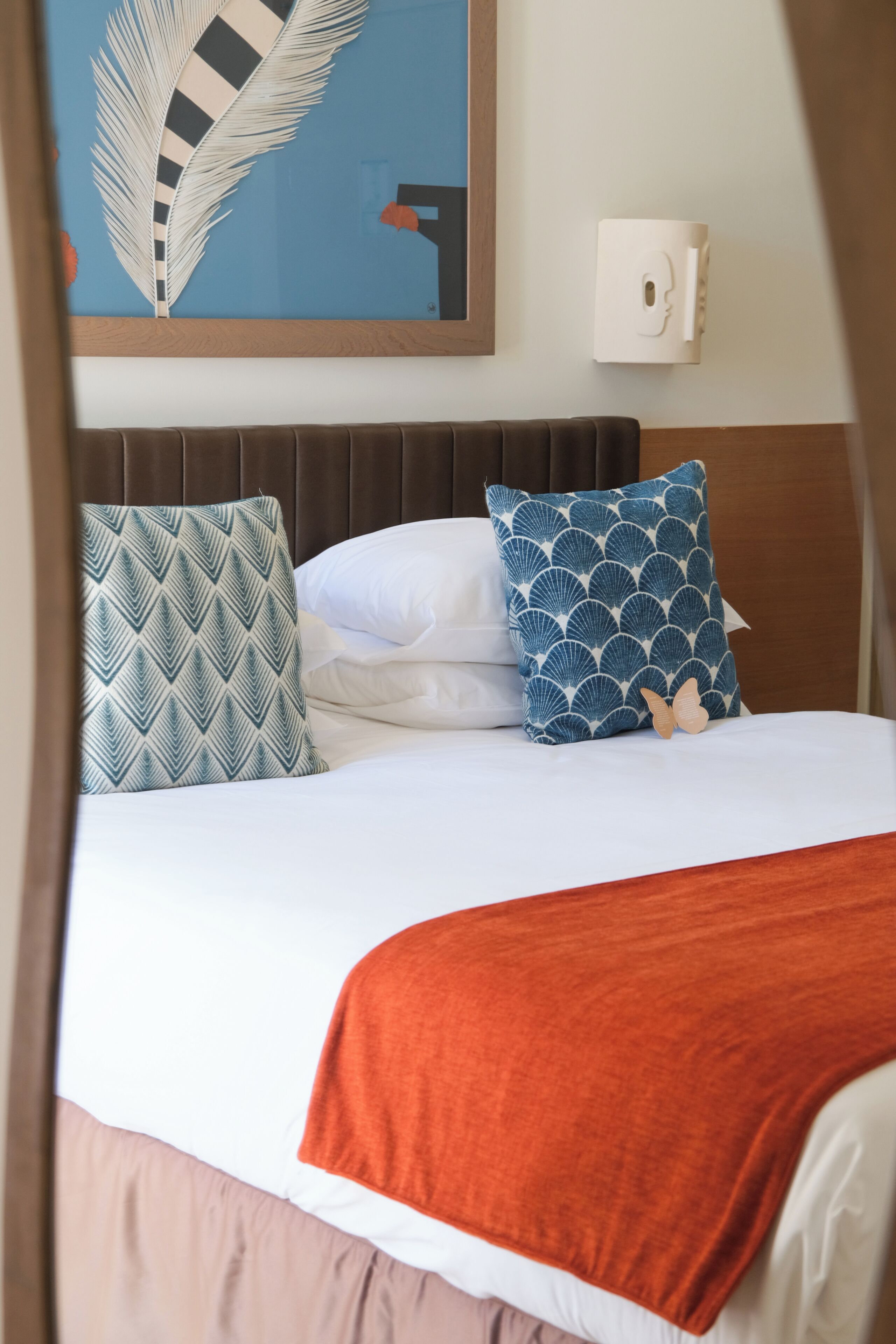 A bed with patterned pillows, a white wall, and a mounted device.
