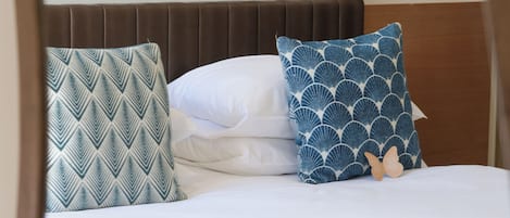 Una cama con almohadones estampados, una pared blanca y un dispositivo montado.