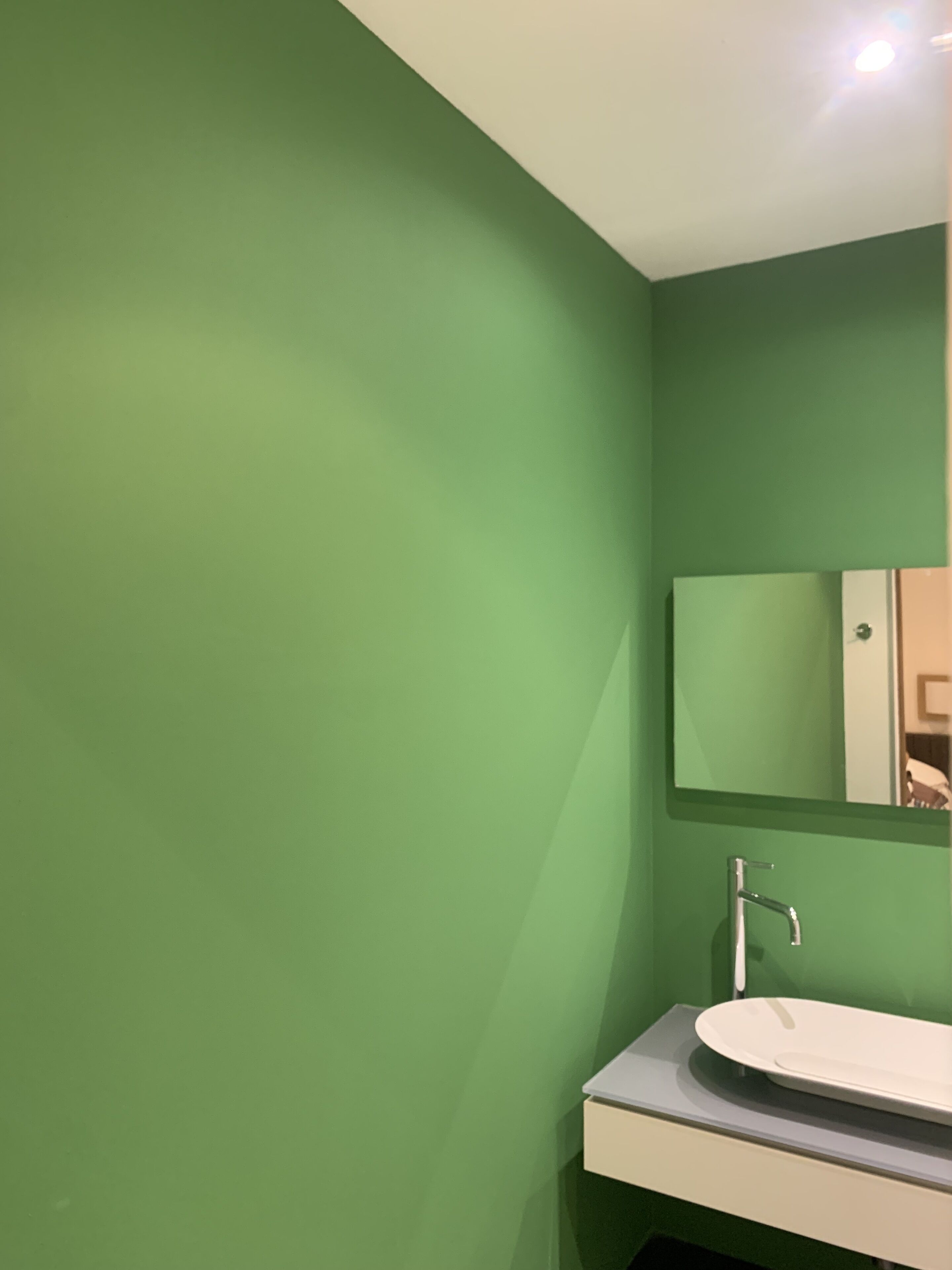 A bathroom with a green wall, a white sink, and a mirror.
