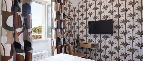 A bedroom with a bed, a desk, a chair, a TV mounted on the wall, and a window with curtains.