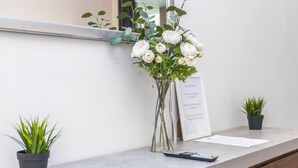 A reception desk with a vase of white flowers, a framed 'No Smoking' sign, and two potted plants. - Point West Apartments Gloucester Road (London)