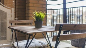 A wooden table with a potted plant, a cushioned bench, and a metal railing on a balcony. - Point West Apartments Gloucester Road (London)