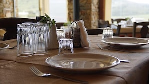 A table set for dining with clear glassware, plates, and cutlery, and a small potted plant. - Ktima Nikola (Karystos)