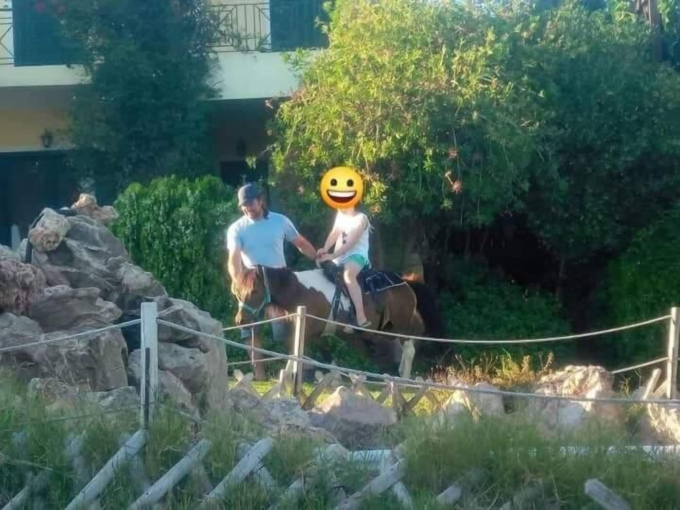 Two people on a horse near a rope barrier in a natural setting with rocks and greenery.