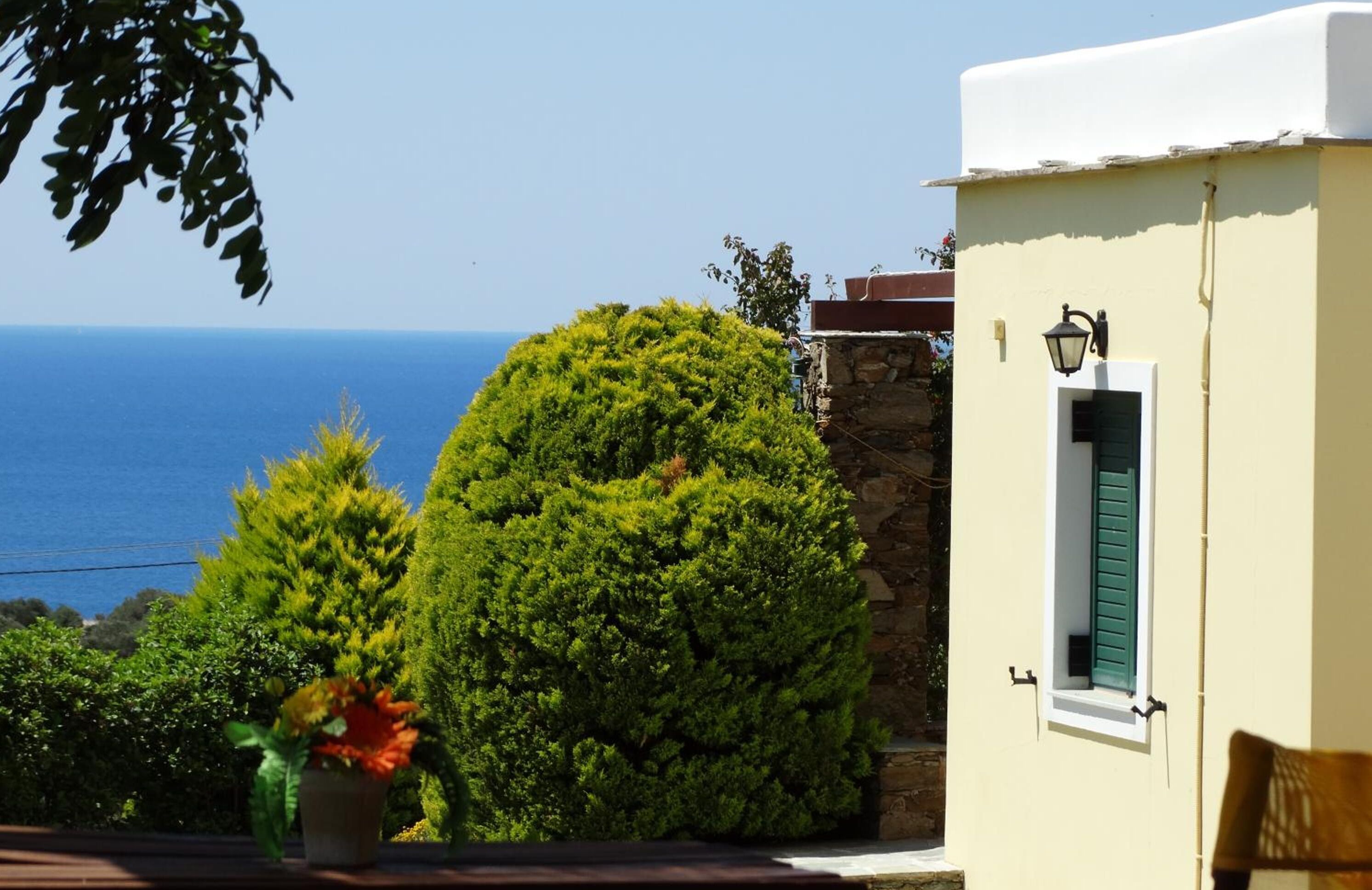 Un edificio costero con pared de piedra, una ventana pequeña con contraventanas verdes y vista al mar.