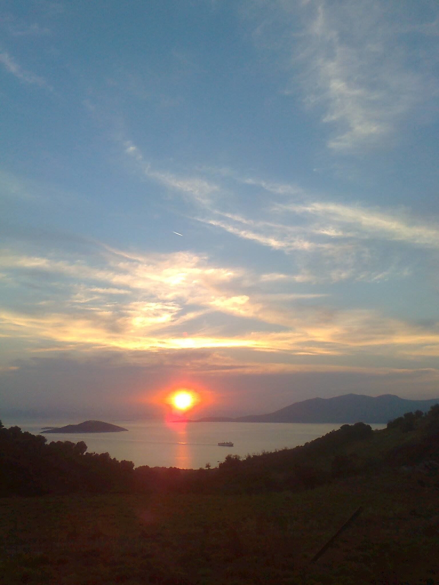 A sunset over a body of water with distant landforms and a clear sky.