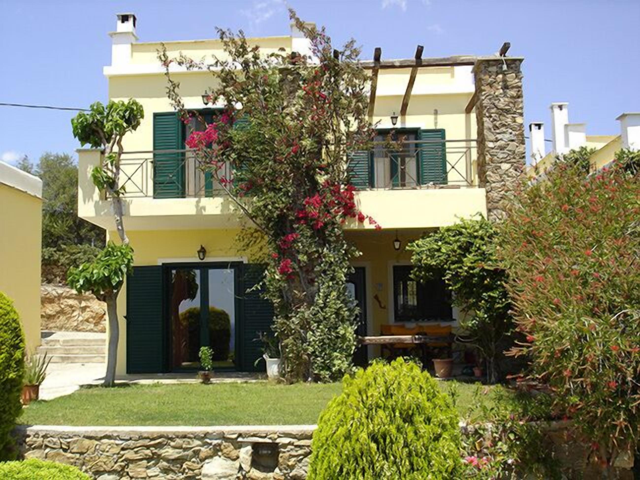 A two-story house with a stone facade, green shutters, and a well-maintained garden.