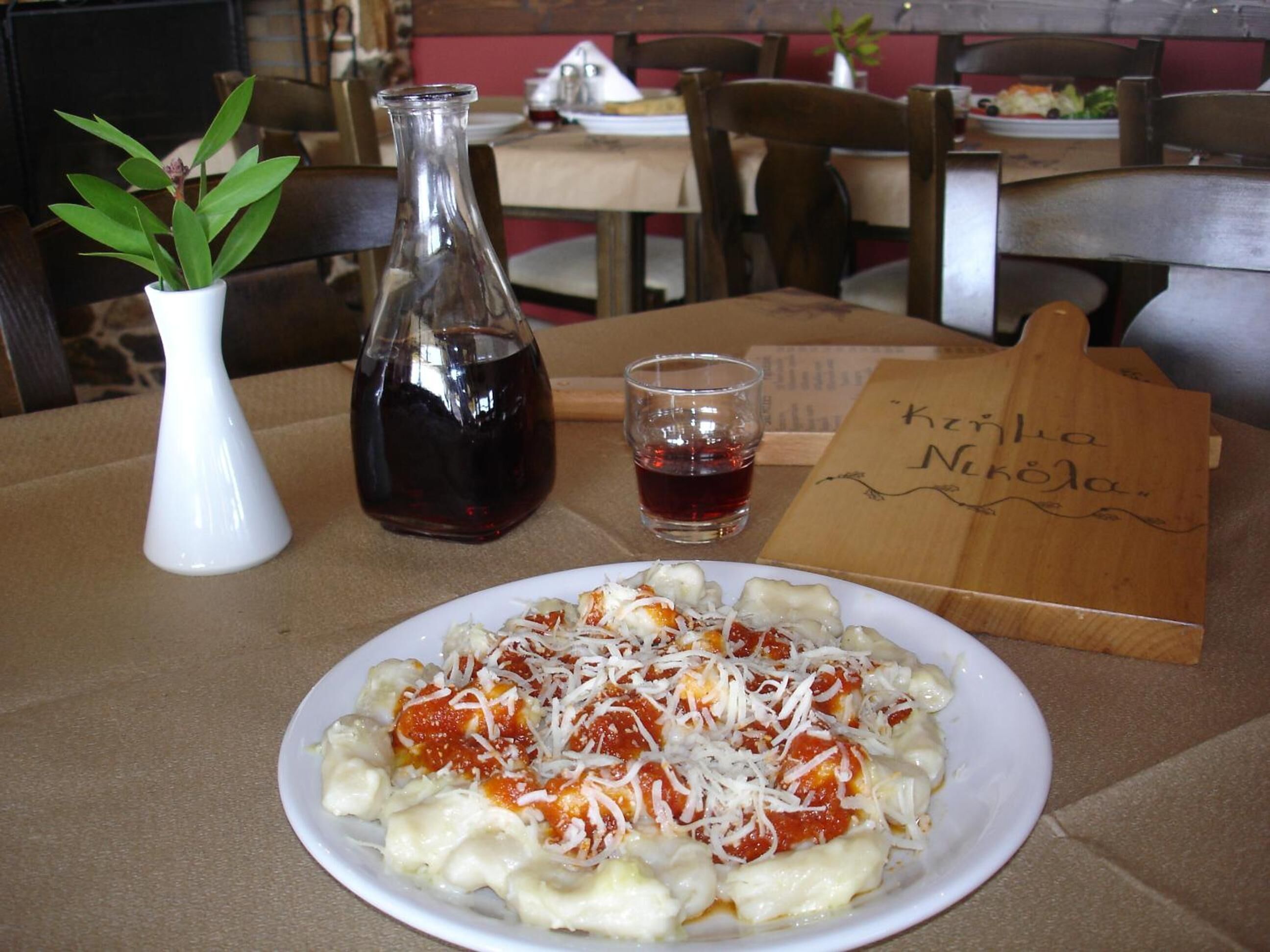 A plate of pasta with tomato sauce and cheese, a glass of red wine, and a wooden menu on a table in a restaurant.