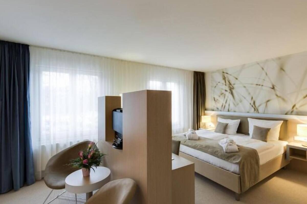 Une chambre d’hôtel avec un lit, un bureau, une chaise et une grande fenêtre avec des rideaux.
