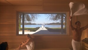 A sauna room with a bench, a large window, and a view of a lake.