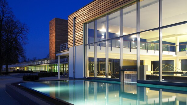 A modern building with a glass facade, a pool, and a staircase leading to an upper level.