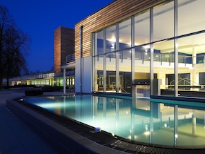 Un edificio moderno con fachada de vidrio, piscina y escalera que lleva a un nivel superior.