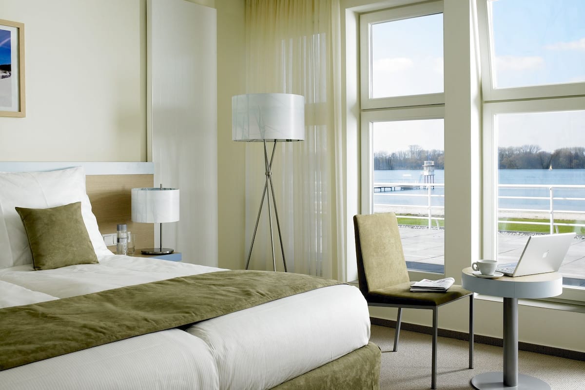 Une chambre d’hôtel avec un lit, une chaise, un bureau avec un ordinateur portable et une vue sur un lac.