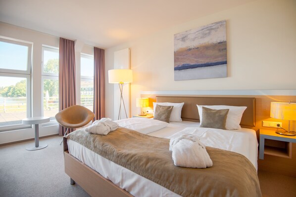 Habitación de hotel con una cama grande, una silla, un escritorio y vistas al exterior.