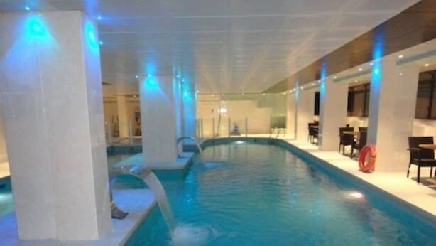 Una piscina interior con agua cristalina, rodeada de columnas y un área de estar con mesas y sillas.