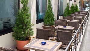 Un área de estar al aire libre con sillas y mesas de mimbre, plantas en macetas y una barandilla.