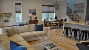 Ein Wohnzimmer mit einer Couch, einem Hocker und einem Essbereich mit Stühlen und einem Tisch.